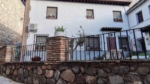 A traditional building with a stone wall in front, a tiled roof, and a metal fence. - Casa Alfonso Toledo - Más que una casa, un hogar (Toledo)
