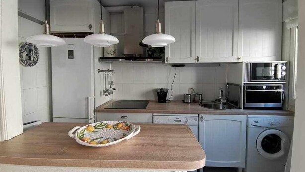 A compact kitchen with white cabinets, a wooden countertop, a built-in oven, and a washing machine. - Casa Alfonso Toledo - Más que una casa, un hogar (Toledo)