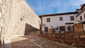 A cobblestone street with a stone wall on one side and a building with a tiled roof and windows on the other. - Casa Alfonso Toledo - Más que una casa, un hogar (Toledo)