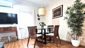 A dining area with a wooden table and chairs, a hanging lamp, a potted plant, and a framed picture on the wall.