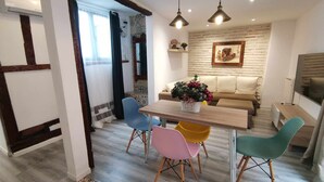 A dining area with a wooden table, colorful chairs, a potted plant, and a sofa in the background.