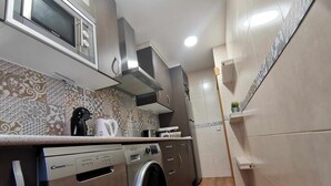 A compact kitchen with a washing machine, microwave, and a coffee maker on the counter.