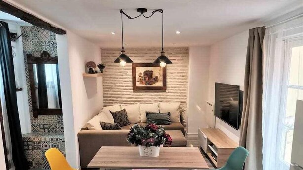 Ein modernes Wohnzimmer mit einem Holzesstisch, bunten Stühlen, einer Couch und einem Fernseher.