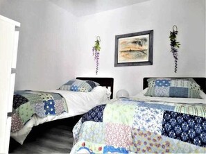 Een slaapkamer met twee bedden, elk voorzien van een gewatteerde spreidek en kussens. Aan de muur hangen twee afbeeldingen in een lijst, een van een landschap en een andere van een plant.
