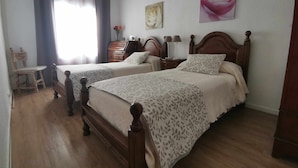 A room with two wooden beds, a wooden chair, a dresser, and a nightstand with lamps. - Casa Cervantes Toledo (Toledo)