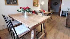 A dining area with a wooden table, chairs, and a vase of flowers. There are paintings on the walls and a radiator in the background. - Casa Cervantes Toledo (Toledo)