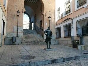 A statue in a plaza with stone steps leading up to a building with arched windows. - Casa Cervantes Toledo (Toledo)