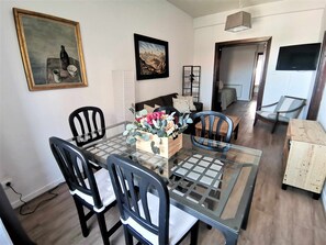Un coin repas avec une table en verre, des chaises noires, un vase de fleurs et des œuvres d’art encadrées accrochées aux murs.