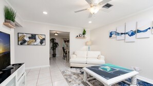 A modern living room with a white sofa, a coffee table with a blue abstract design, and a television on a stand. - Let's Spend Some Time Together (Wellington)