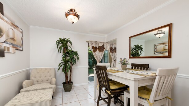 A dining area with a white table, two wooden chairs, a potted plant, and a mirror on the wall. - Let's Spend Some Time Together (Wellington)