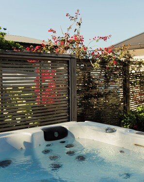 A hot tub with a wooden fence and flowering plants in the background.