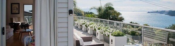 A balcony with a view of the sea, outdoor seating, and potted plants.