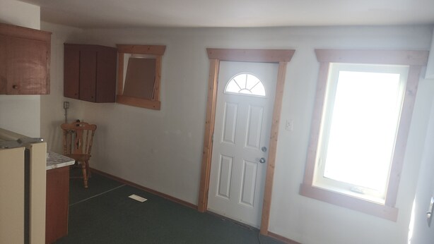 A narrow hallway with a wooden door, a window, and a small kitchen area with a refrigerator and a chair. - Retro Cowboy Country Style Great Ranchhand Worker (Bethune)