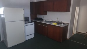 A compact kitchen with a refrigerator, stove, and wooden cabinets. - Retro Cowboy Country Style Great Ranchhand Worker (Bethune)