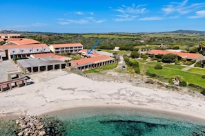 An aerial view of a coastal hotel with multiple buildings, a sandy beach, and clear turquoise waters.