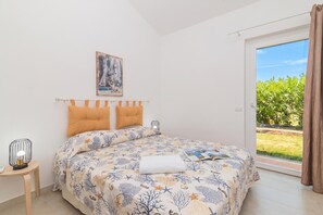 Un dormitorio con una cama, una mesita de noche, una ventana con vistas a la vegetación y un cuadro en la pared.