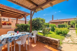 A covered patio with a table and chairs, a stone wall, and a garden path.