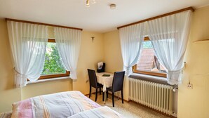 Quarto com duas camas, uma mesa com cadeiras, um radiador e uma janela com cortinas.