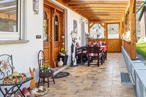 Un patio coperto con tavolo e sedie in legno, una sedia in vimini e oggetti decorativi.