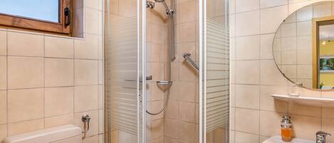 Une salle de bain avec une douche à parois de verre, des toilettes, un lavabo avec un miroir et une fenêtre située au-dessus des toilettes.