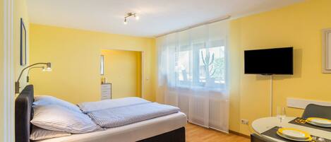 Ein Hotelzimmer mit Bett, einem Esstisch mit Stühlen, einem Fernseher und einem Fenster mit Vorhängen.