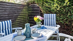 A patio table with a pitcher, cups, and plates, surrounded by striped chairs.