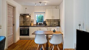 A compact kitchen with a stove, oven, and coffee maker, a dining table with chairs, and a window with a view of greenery.