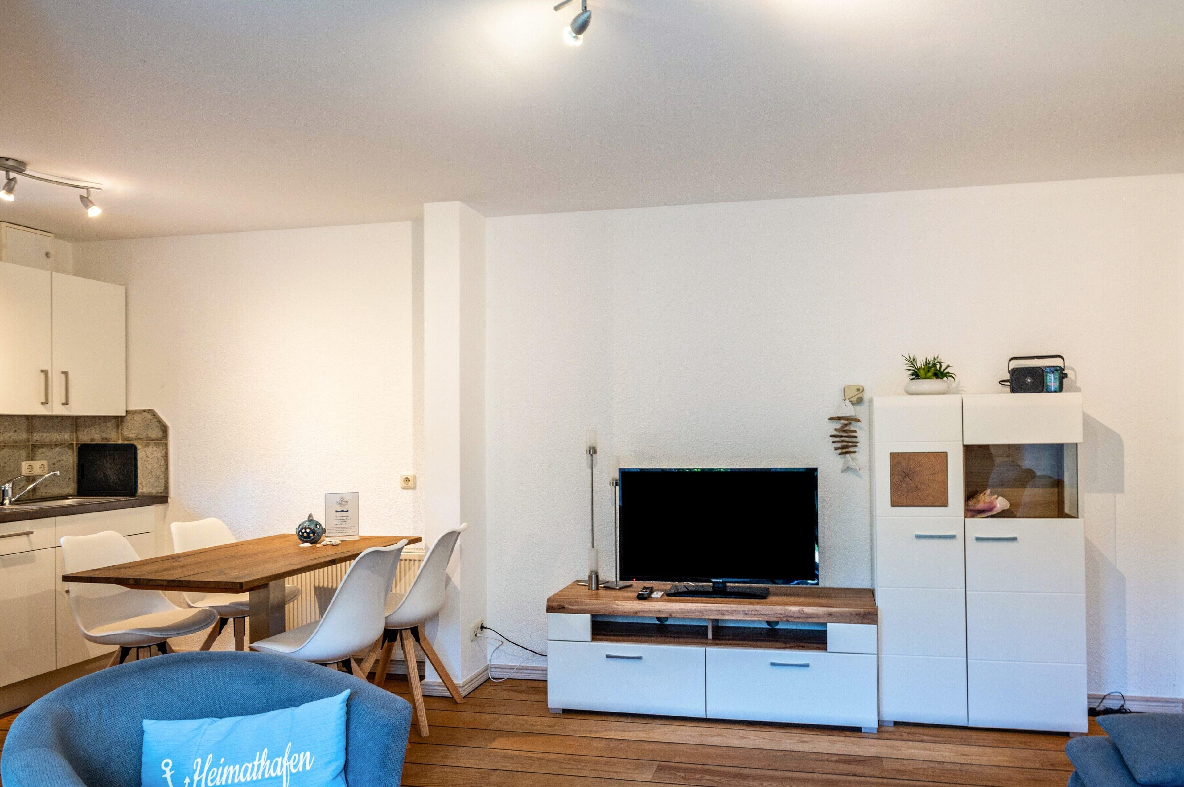 Un soggiorno moderno con televisore a schermo piatto, mobili bianchi, un'area pranzo con tavolo e sedie in legno e un divano blu.