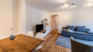 A modern living room with a wooden dining table, a grey sofa, and a television.