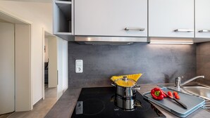 Une cuisine moderne avec un fourneau, une casserole de spaghettis et une planche à d écouper avec des légumes.