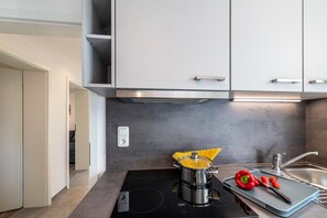 Uma cozinha moderna com fogão, um bule de espaguete e uma tábua de corte com legumes.