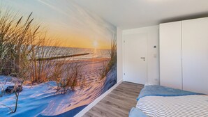 Une chambre avec une fresque murale représentant une plage, un lit avec une literie à rayures et une armoire blanche.