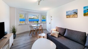 Un salon moderne avec un canapé, une table à manger et des chaises, un téléviseur et des œuvres d’art accrochées aux murs.