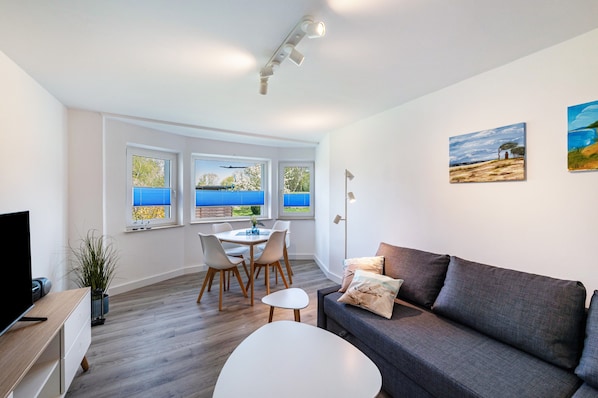 A modern living room with a sofa, a dining table with chairs, a TV, and artwork on the walls.