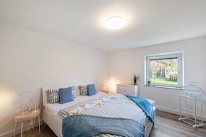A bedroom with a bed, bedside table, lamp, window, and a drying rack.