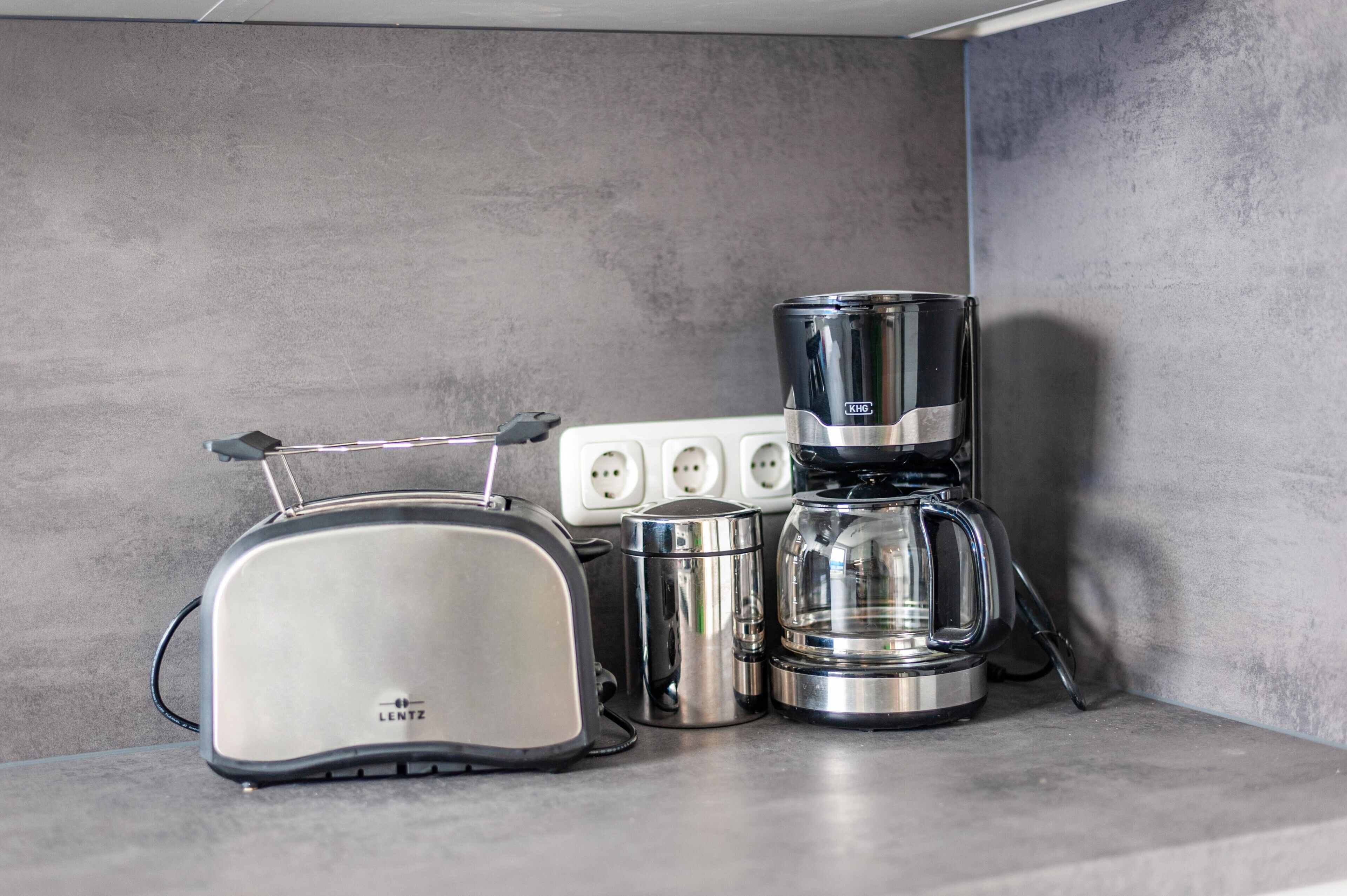 Een aanrecht met een LENTZ-toaster, een KOH koffiezetapparaat en een roestvrijstalen bak.