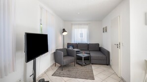 A living room with a flat-screen TV, a gray sofa, a small table, and a lamp.