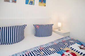 Ein Bett mit gestreifter Bettwäsche, ein Nachttisch mit Lampe und Wandbilder.