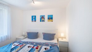 A bedroom with a bed, two bedside tables, a window with curtains, and three wall-mounted paintings.