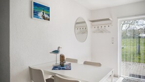 A white table with chairs, a seagull decoration, a painting, a mirror, and a window with a view of greenery.