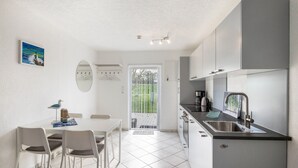 A modern kitchen with white cabinets, a dining table with chairs, and a view through a glass door.