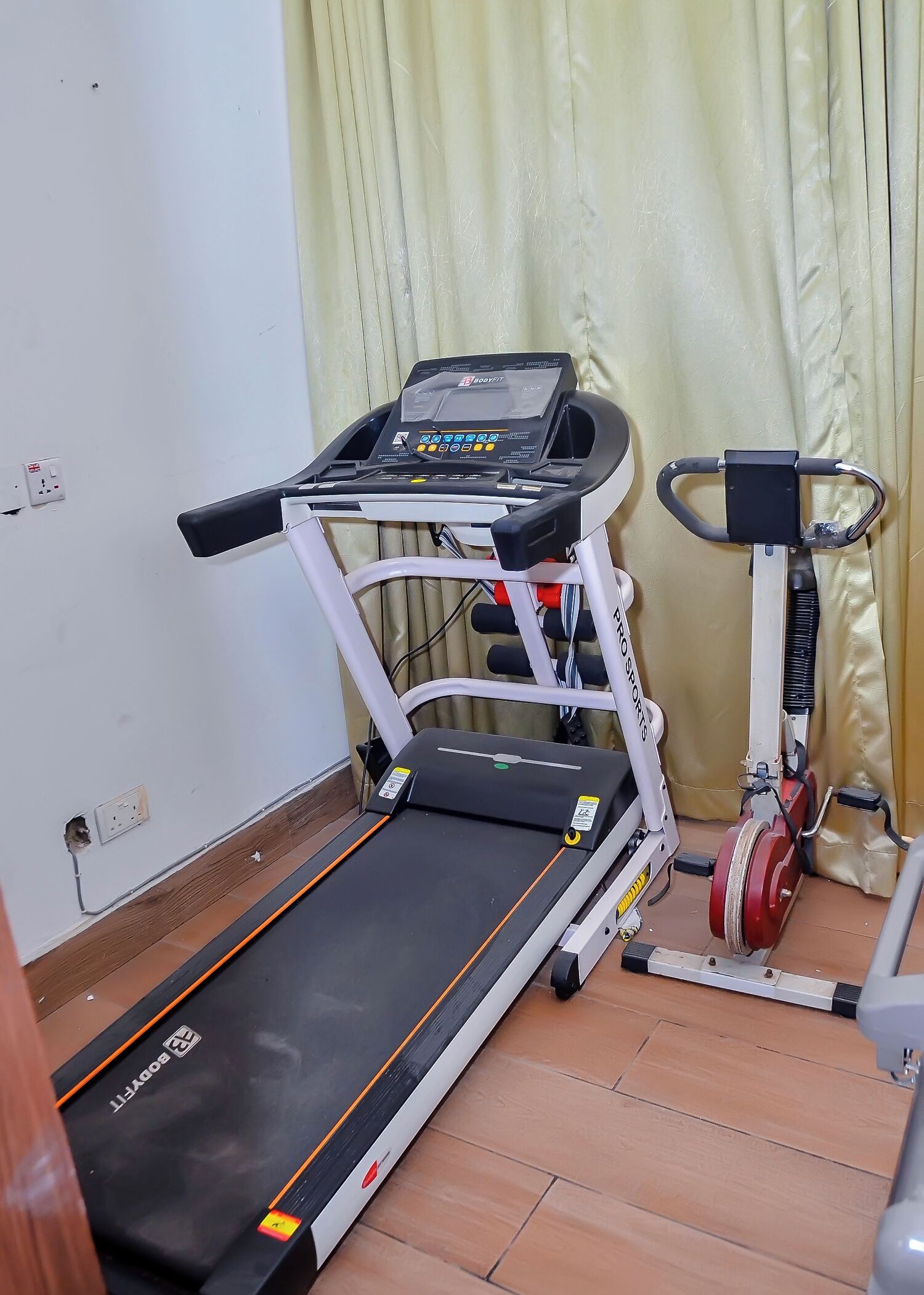 A treadmill and a stationary bike in a room with a tiled floor and a curtain.