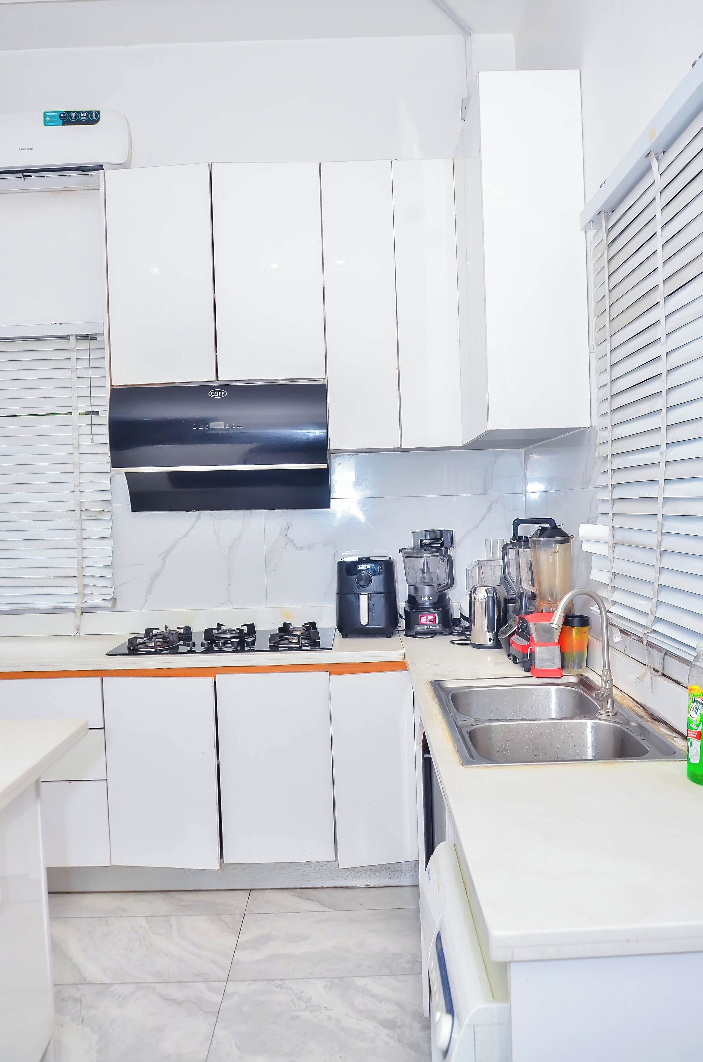 A modern kitchen with white cabinets, a stainless steel sink, a gas stove, and various appliances including a coffee maker and blender.