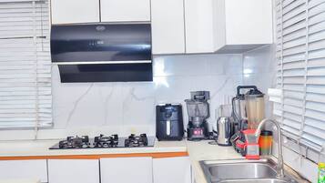 A modern kitchen with white cabinets, a stainless steel sink, a gas stove, and various appliances including a coffee maker and blender.