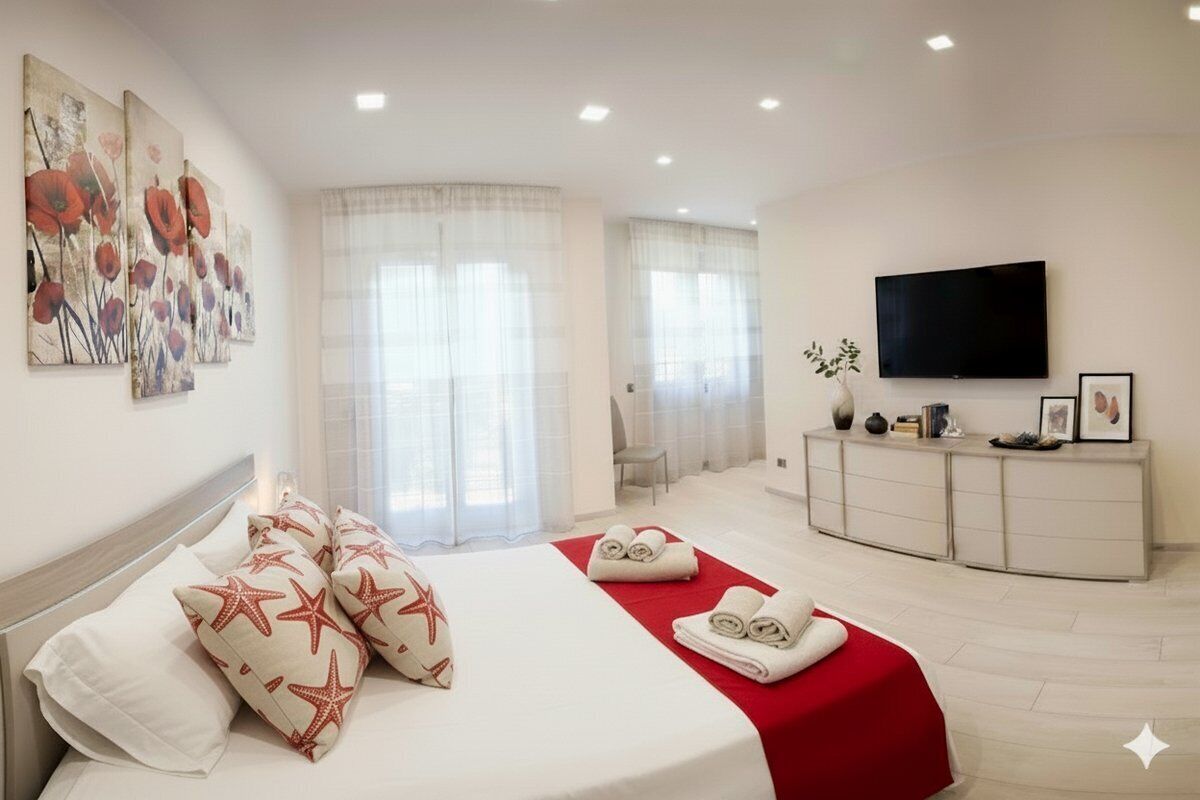 A hotel room with a bed, a TV, a desk, and a window with curtains.