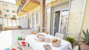 Un patio al aire libre con una mesa lista para comer, rodeado de plantas en macetas y mobiliario de exterior.