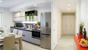 Una cocina moderna con armarios blancos, electrodomésticos de acero inoxidable y un comedor con mesa y sillas.