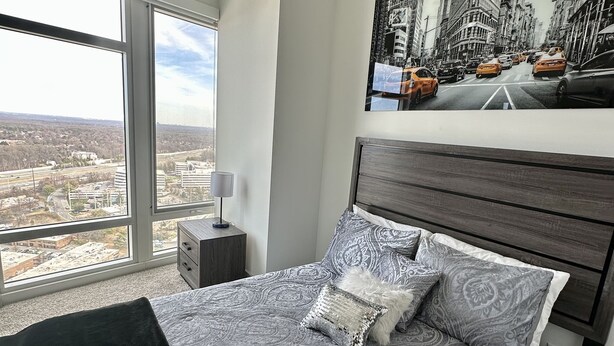 Un dormitorio con una cama grande, una mesita de noche, una lámpara y un cuadro de un paisaje urbano en la pared.