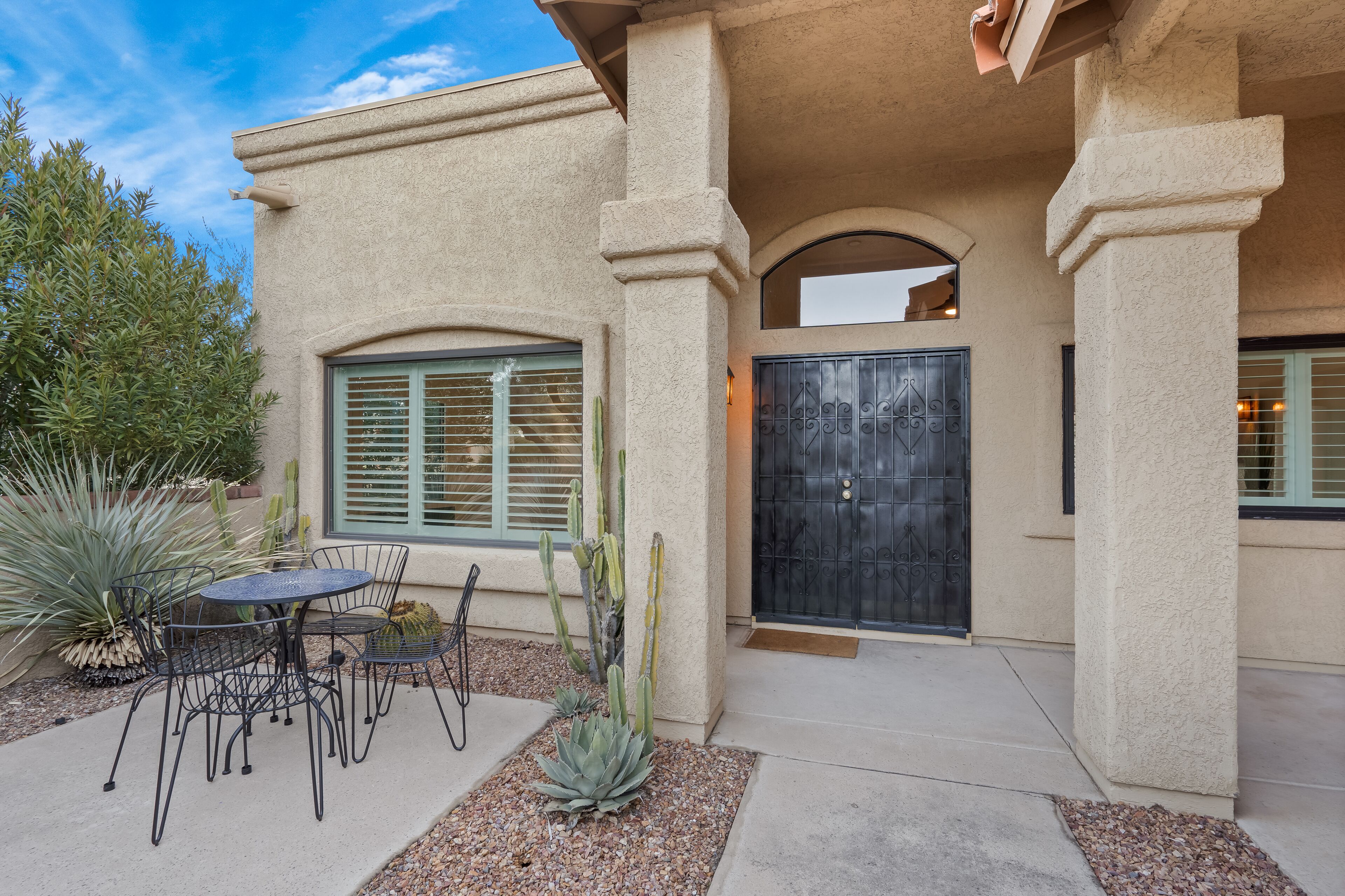 A building with a stucco exterior, a black metal door, and a patio with a table and chairs.