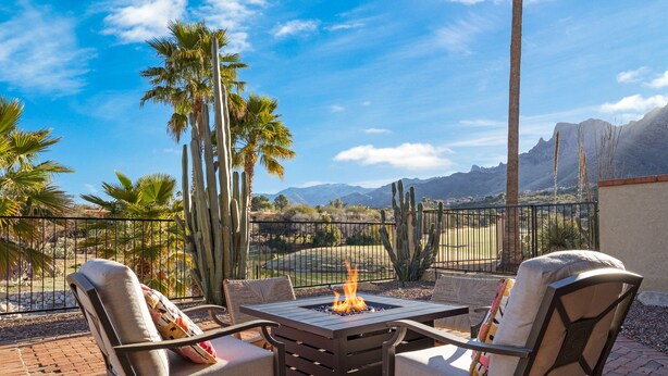 A patio with a fire pit table and chairs, surrounded by cacti and palm trees, with mountains in the background. - El Conquistador/Golf+Mnt+LakesVIEWS/Sleeps4 (Oro Valley)